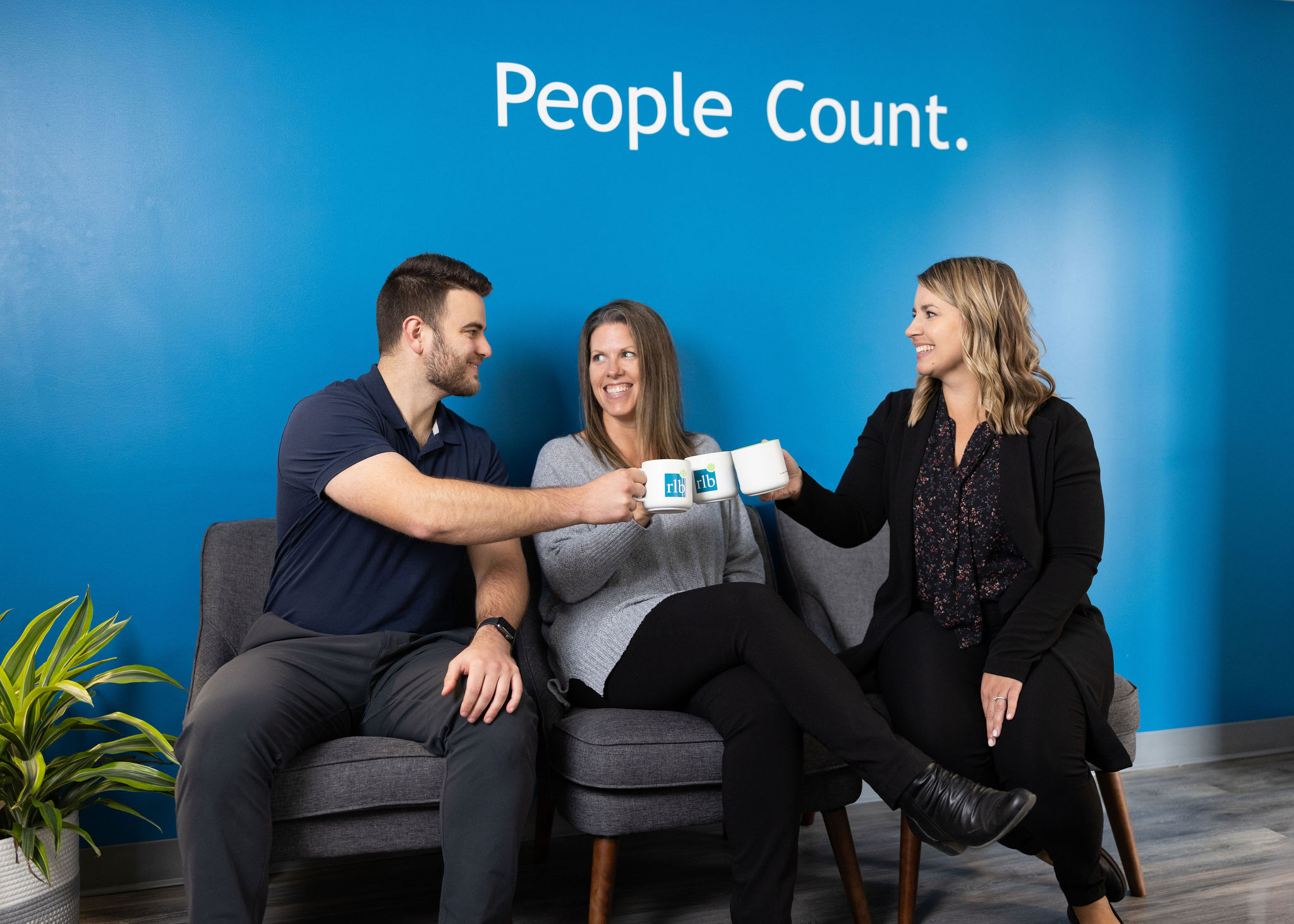 Three people sitting on chairs holding coffee cups and giving cheers.